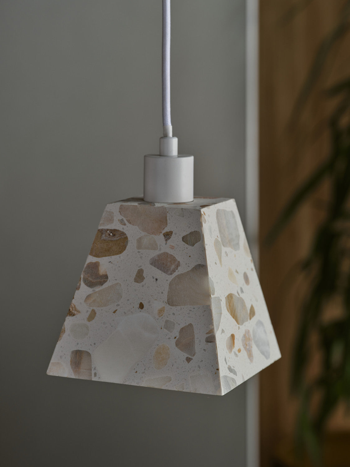 Gros plan sur l'abat-jour carré en terrazzo beige et blanc, suspendu près d'une plante.