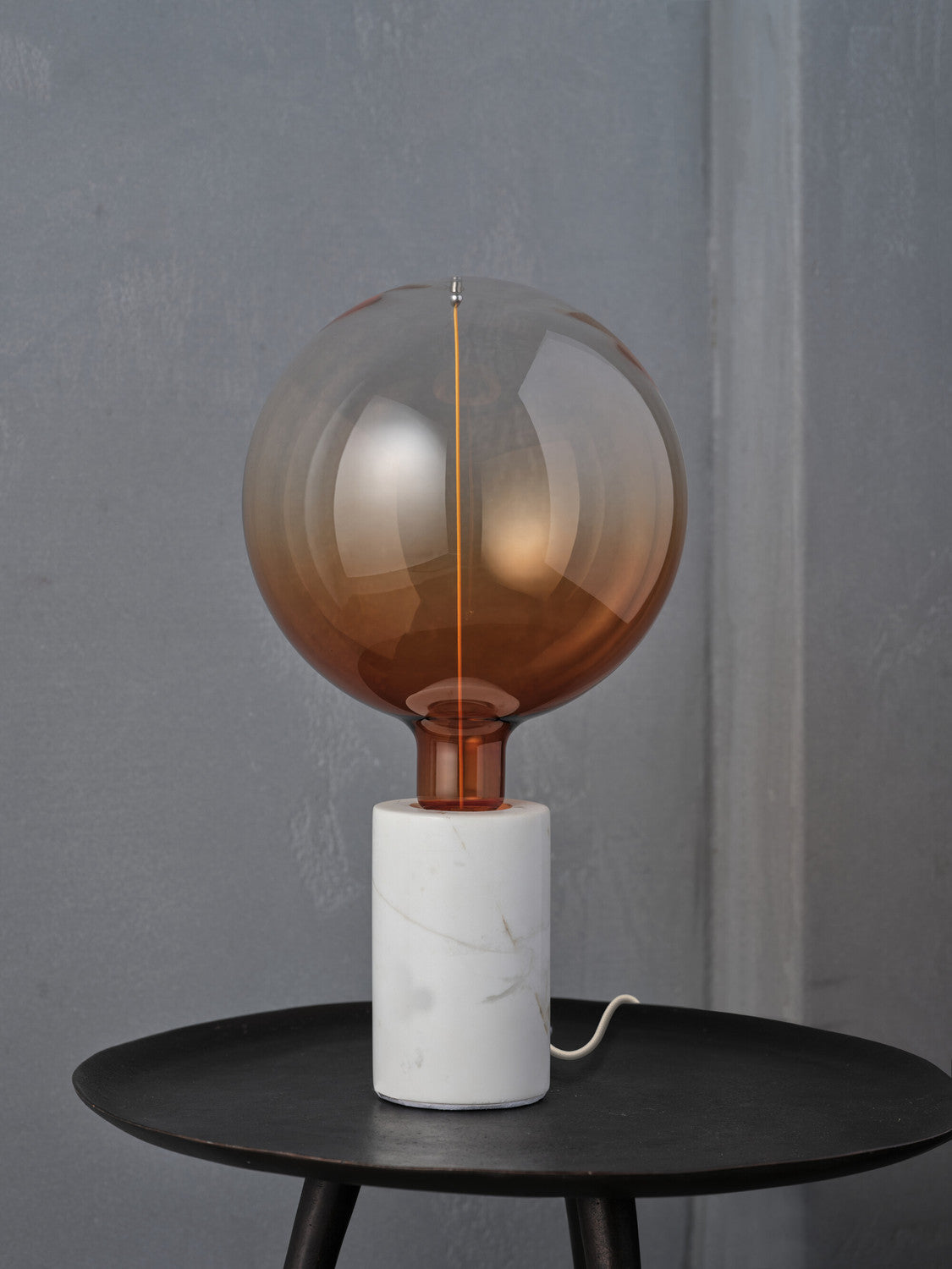 Gros plan de la lampe sur pied en marbre avec ampoule globe ambrée.