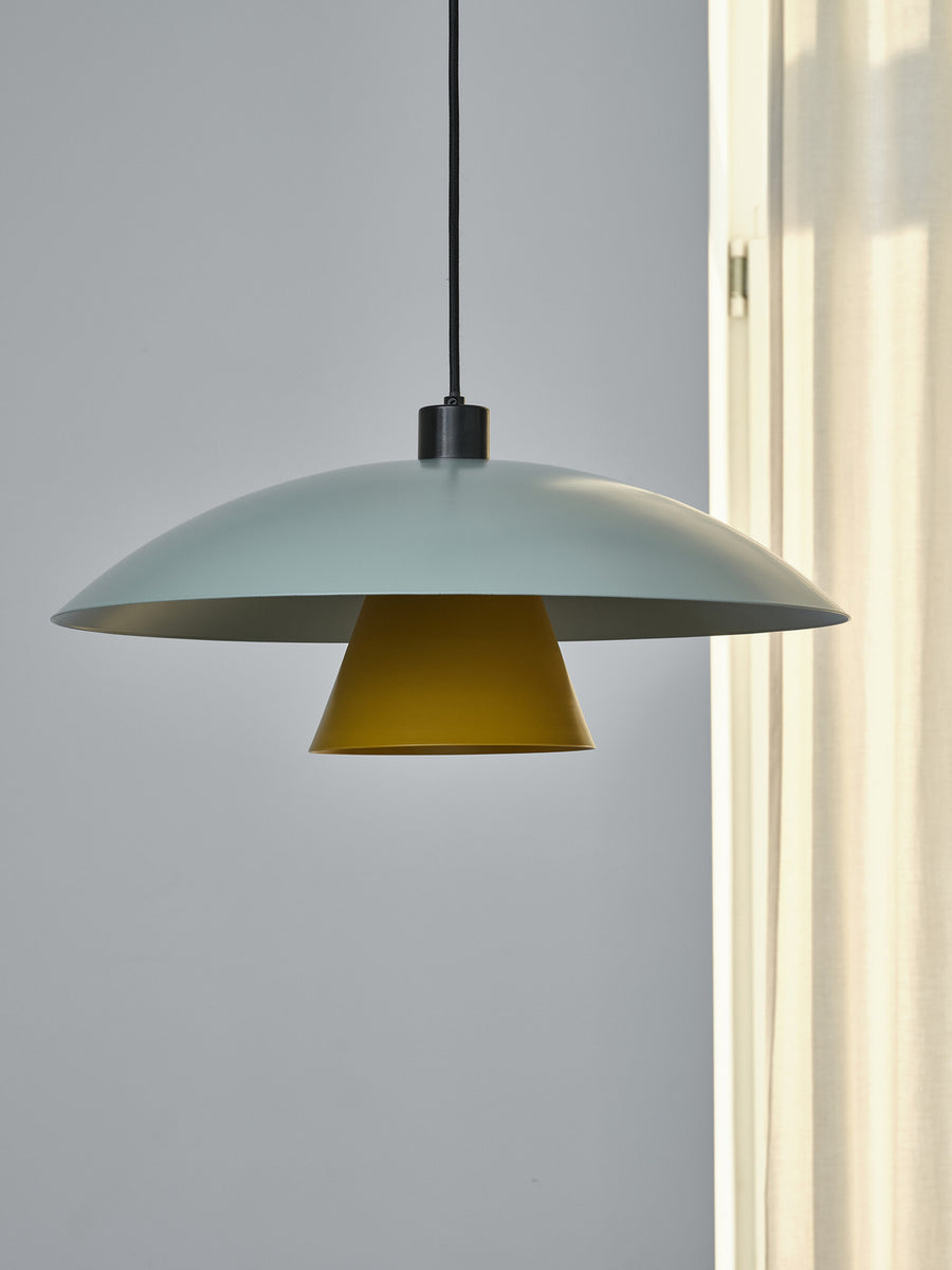 Détail de l'abat-jour vert et du cône jaune près d'une fenêtre lumineuse.