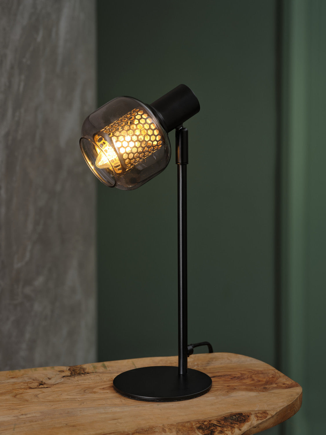 Lampe allumée posée sur une table en bois brut devant un mur vert