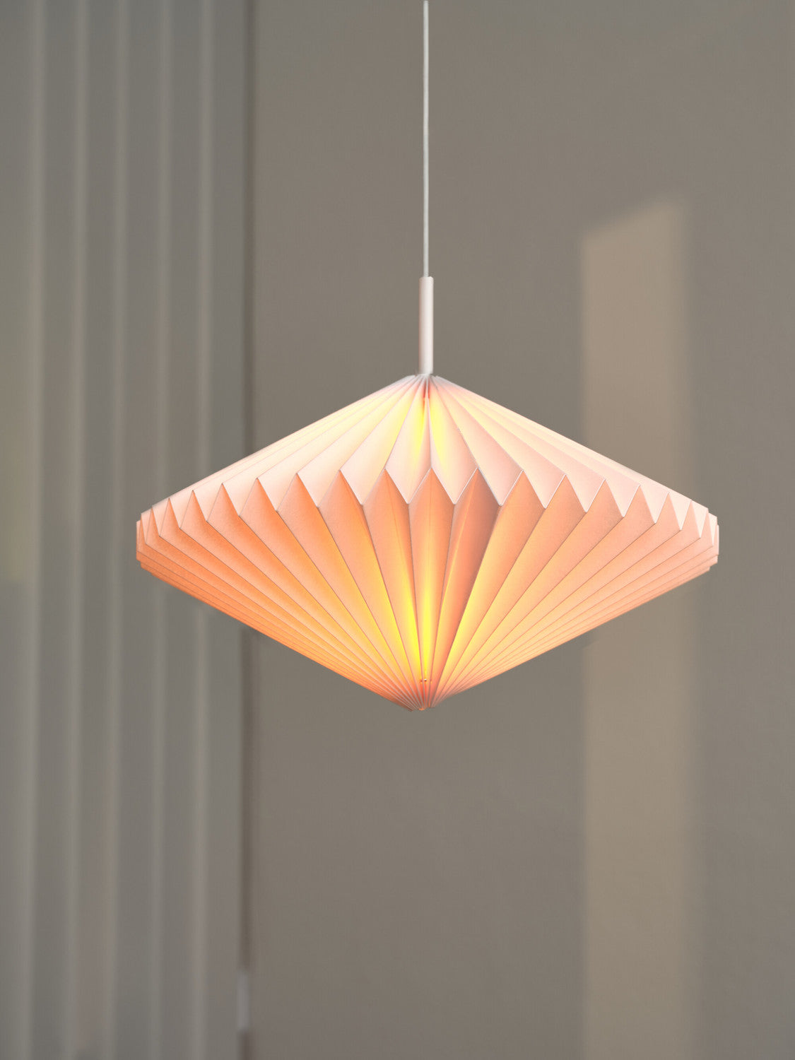 Détail du luminaire allumé, facettes plissées diffusant une lueur orangée douce