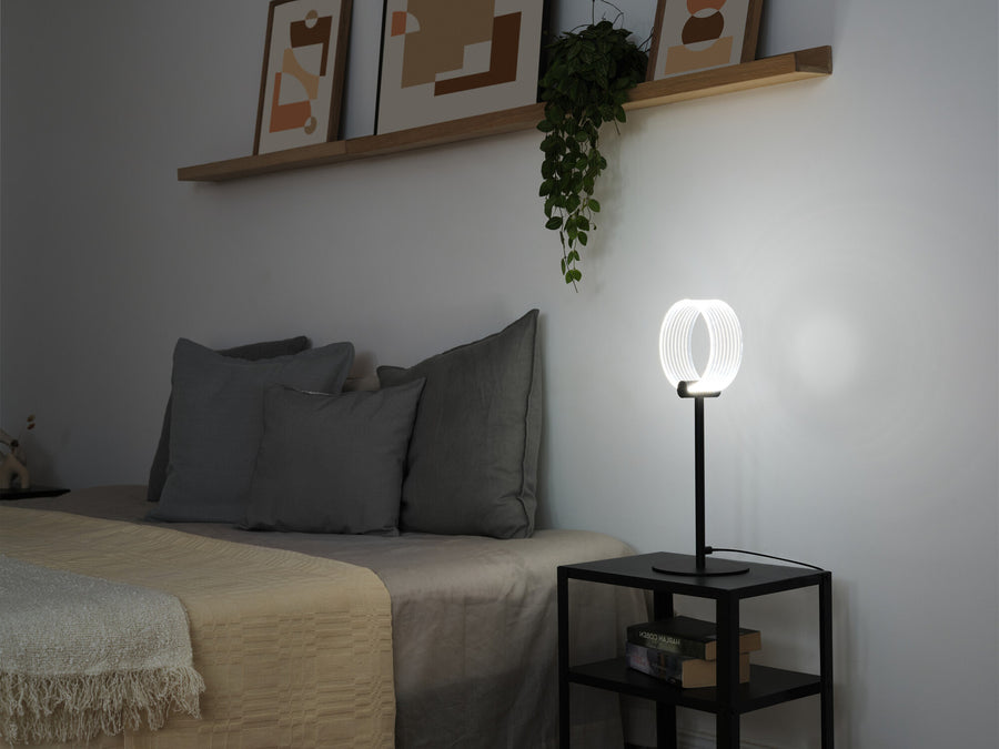 Mise en ambiance dans une chambre avec la lampe allumée près du lit.