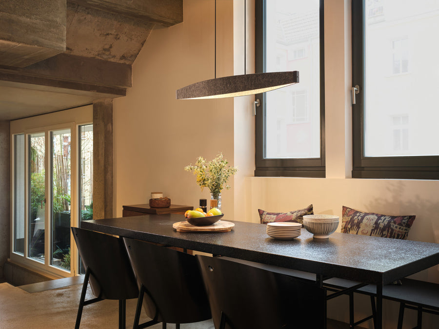 Suspension linéaire anthracite éclairant une grande table dans une salle à manger.