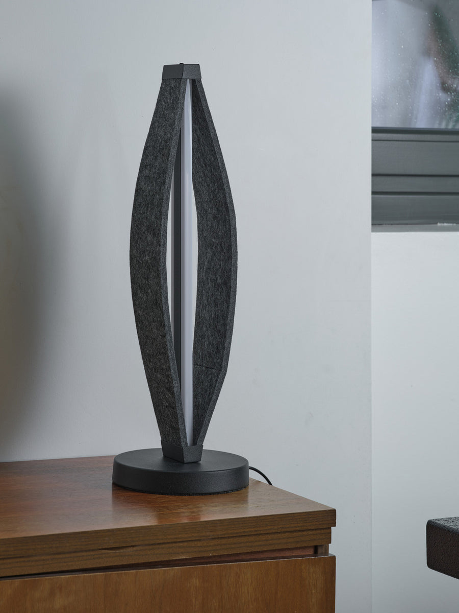 Lampe à poser éteinte sur un meuble en bois, devant un mur blanc et une fenêtre.