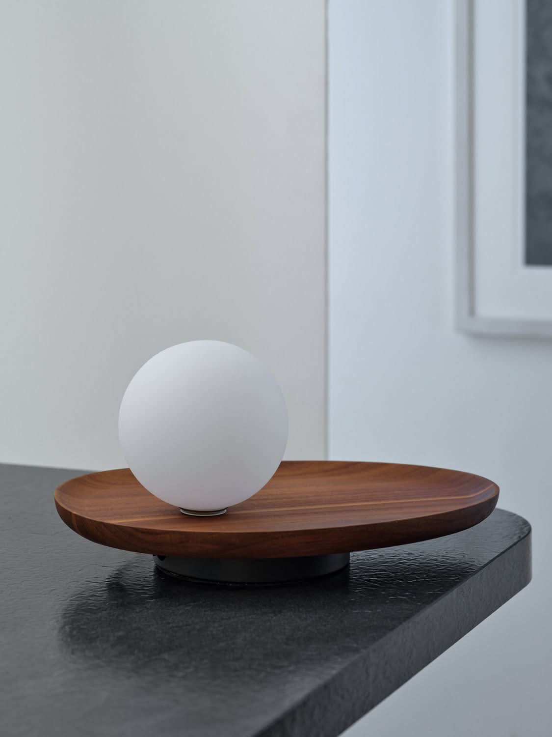 Vue rapprochée du globe blanc et du plateau en bois, posés sur une table sombre.