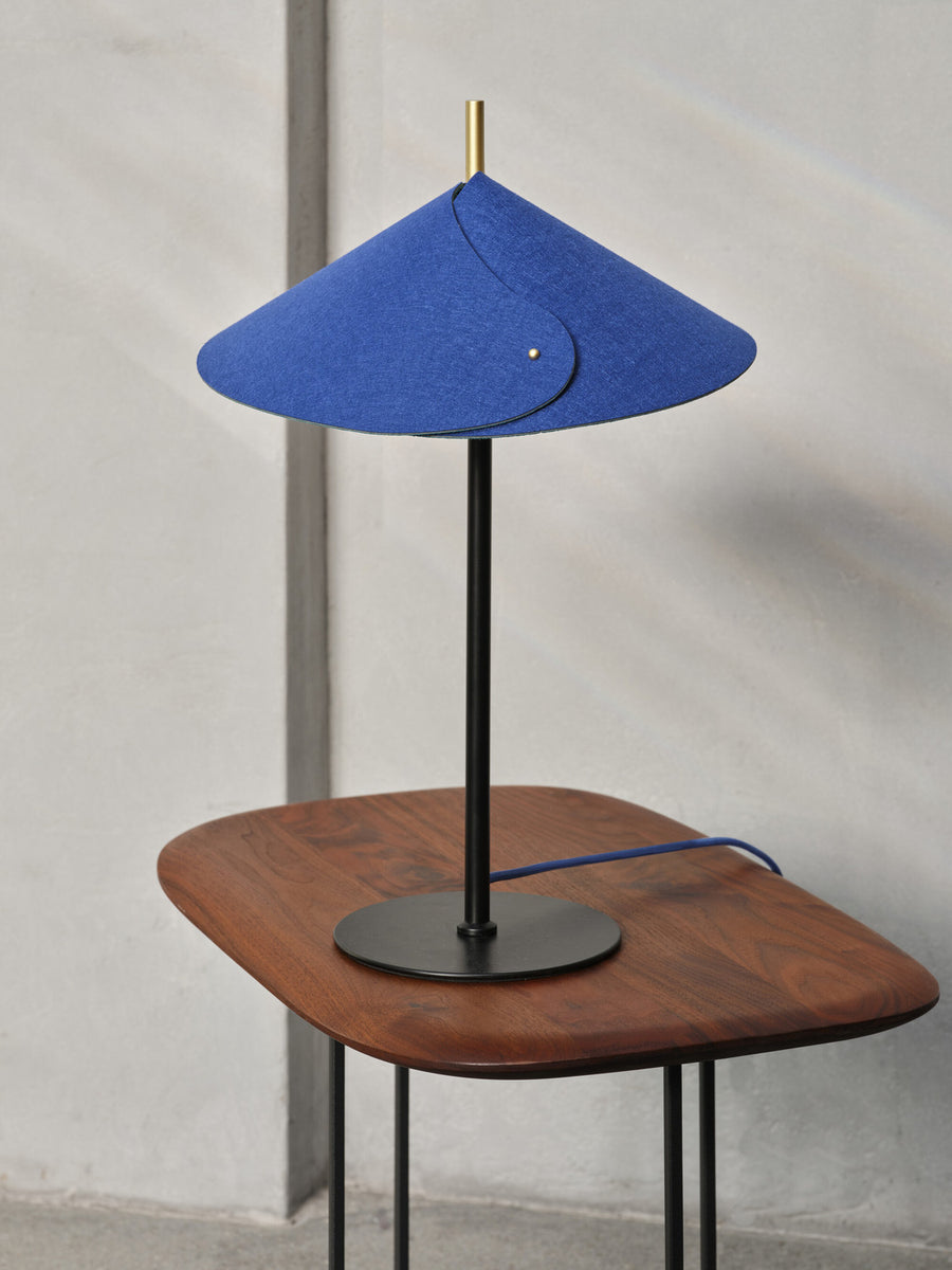 Gros plan de la lampe sur table en noyer, câble bleu et pied noir.
