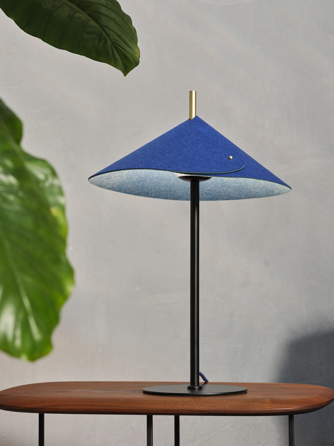 Lampe bleue sur console en bois, feuillage flou et intérieur clair de l’abat-jour.
