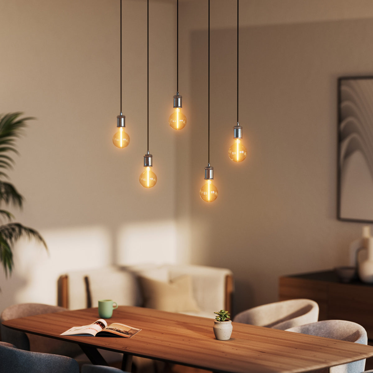Mise en ambiance au-dessus d'une table en bois avec cinq suspensions noires allumées à hauteurs différentes.