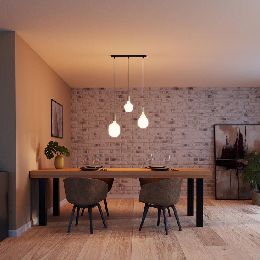 Salle à manger avec trois suspensions dorées alignées au-dessus d'une table en bois.