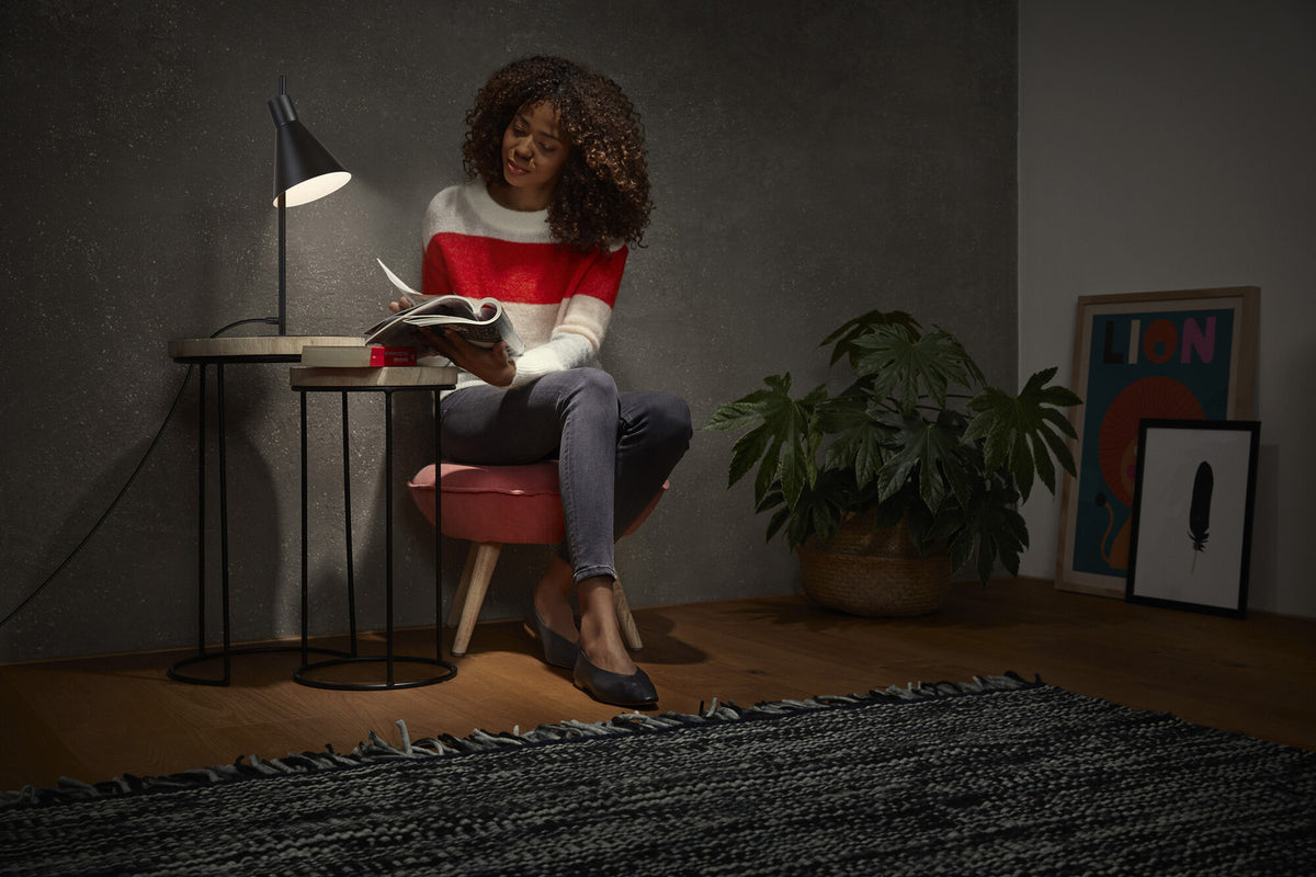 Mise en ambiance : femme lisant près de la lampe allumée sur table.