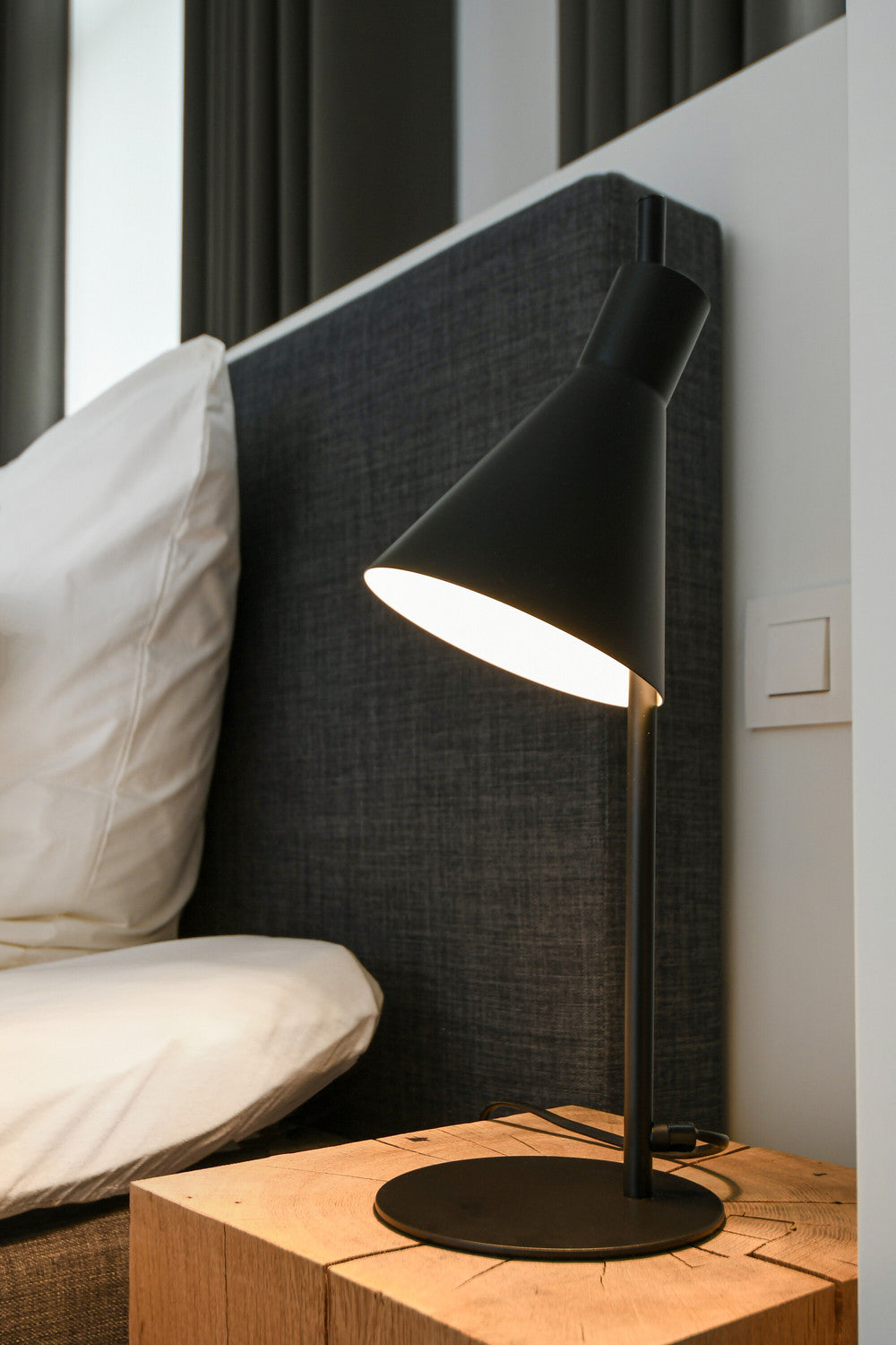 Détail de la lampe allumée près d'un lit, base sur chevet en bois.