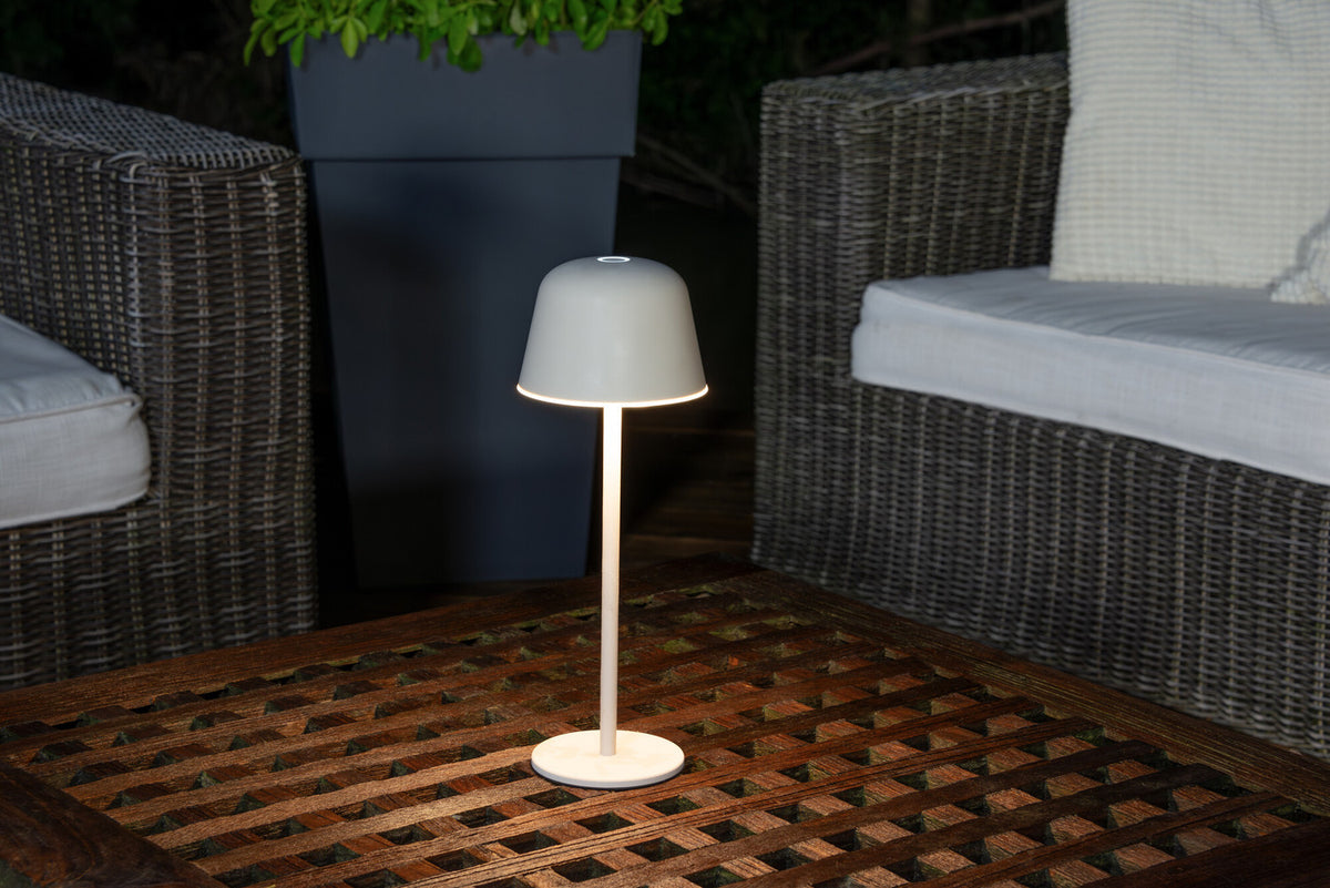 Lampe sans fil posée sur une table basse en bois, entre fauteuils en résine tressée.