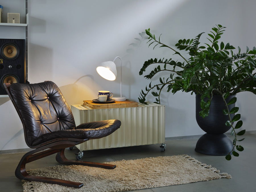 Lampe posée sur un meuble bas près d’un fauteuil en cuir, ambiance salon.
