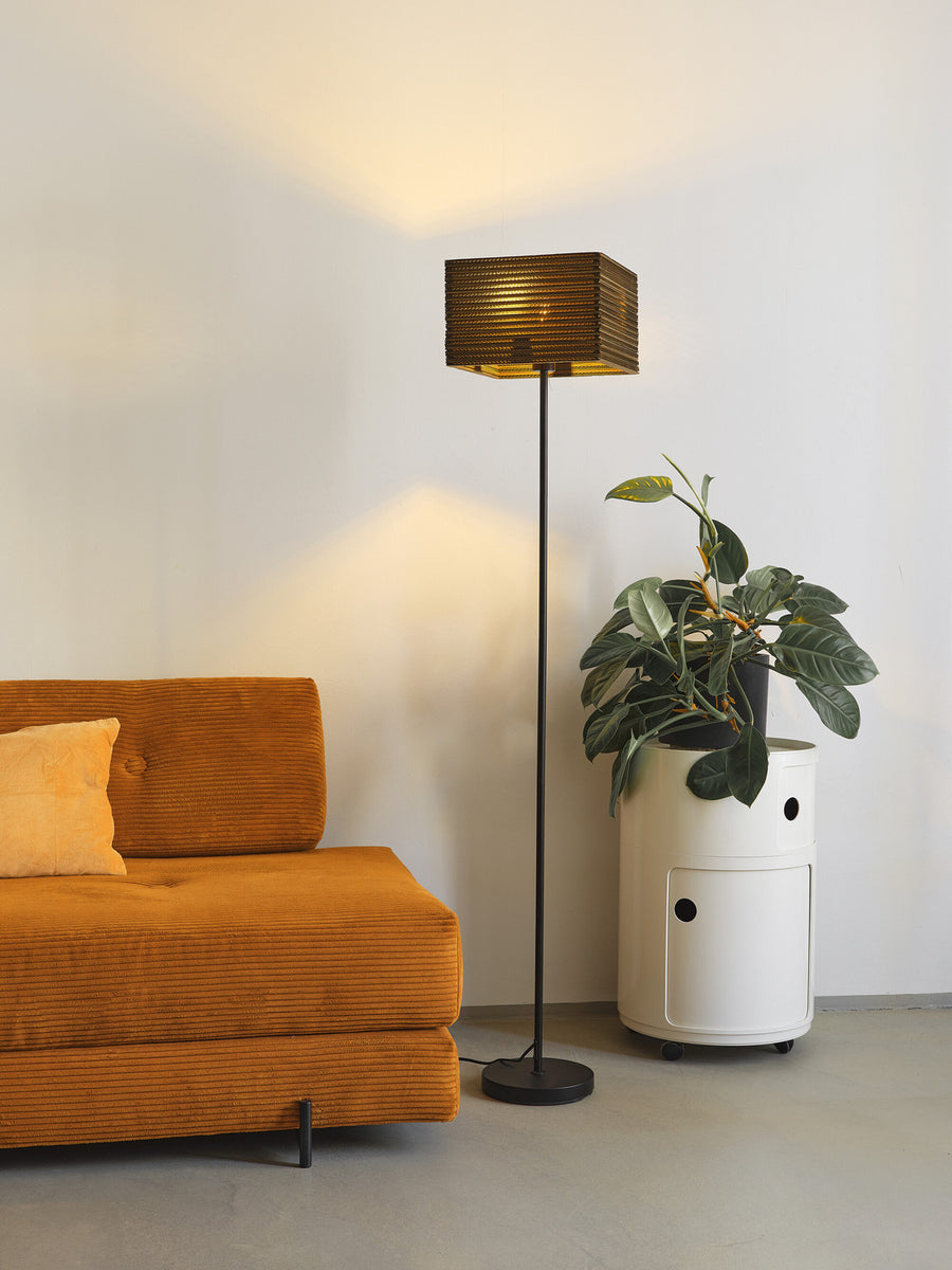 Lampadaire éclairé près d'un canapé orange et d'une plante verte.