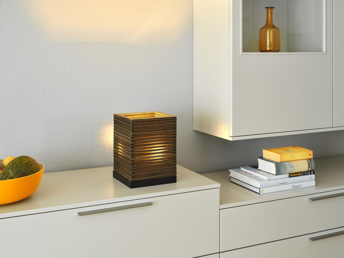 Lampe allumée sur un meuble bas, près d’un bol orange et de livres empilés.