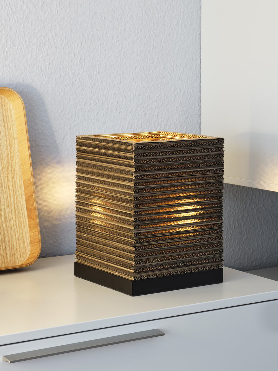 Vue rapprochée de la lampe allumée, posée près d’un plateau en bois clair.