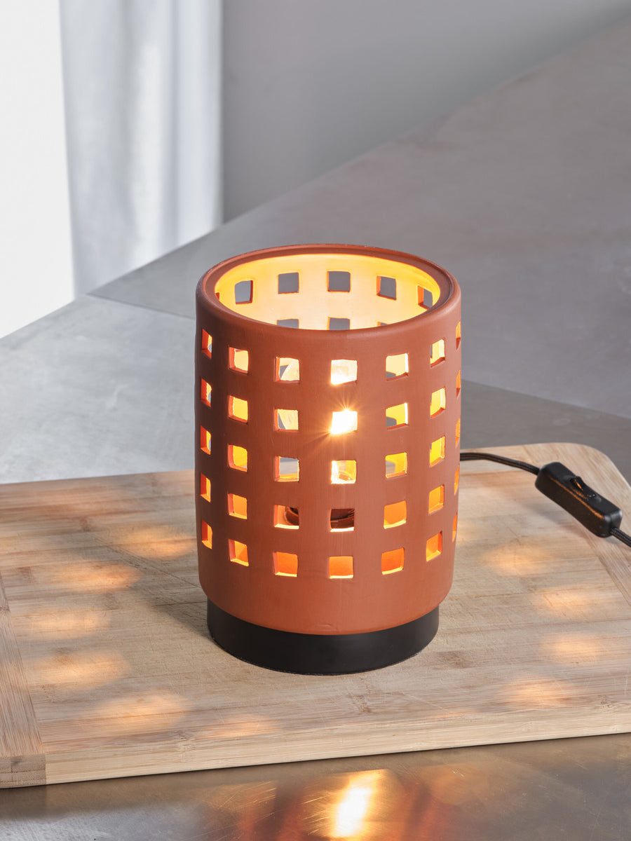 Gros plan sur la lampe allumée, motifs carrés projetant une lumière chaude sur le bois.