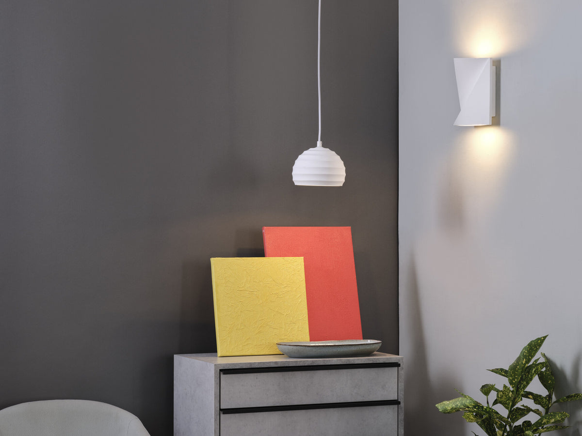 Mise en ambiance intérieure avec applique murale allumée à droite et suspension blanche au centre.