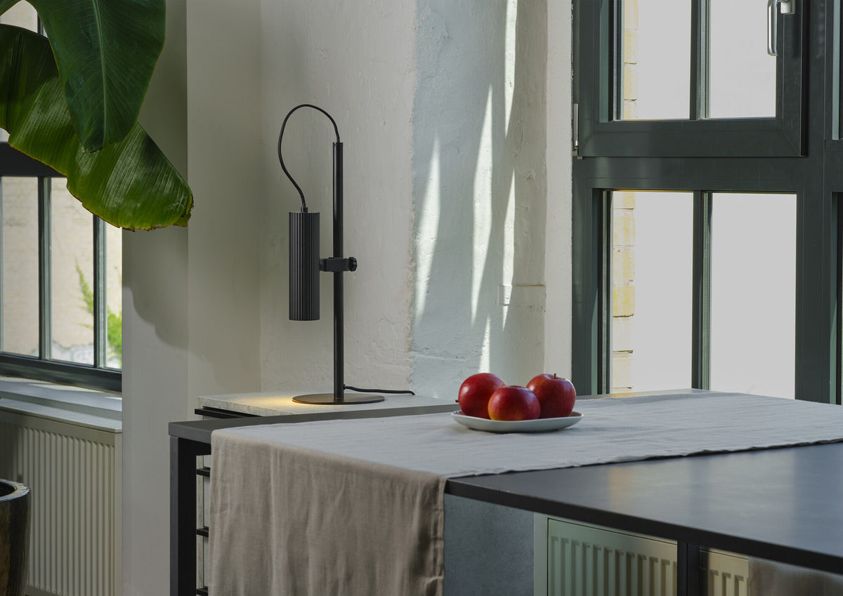 Mise en ambiance sur plan de travail, lampe noire près d'une fenêtre et de fruits