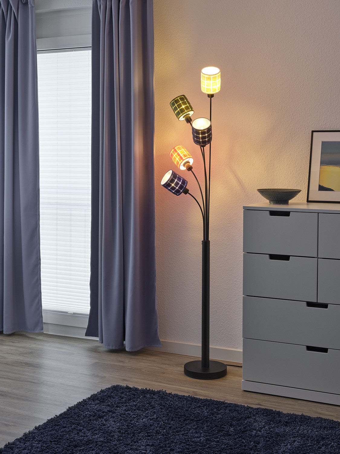 Détail du lampadaire aux cinq abat-jours tressés, près d'une commode grise et d'un tapis bleu.