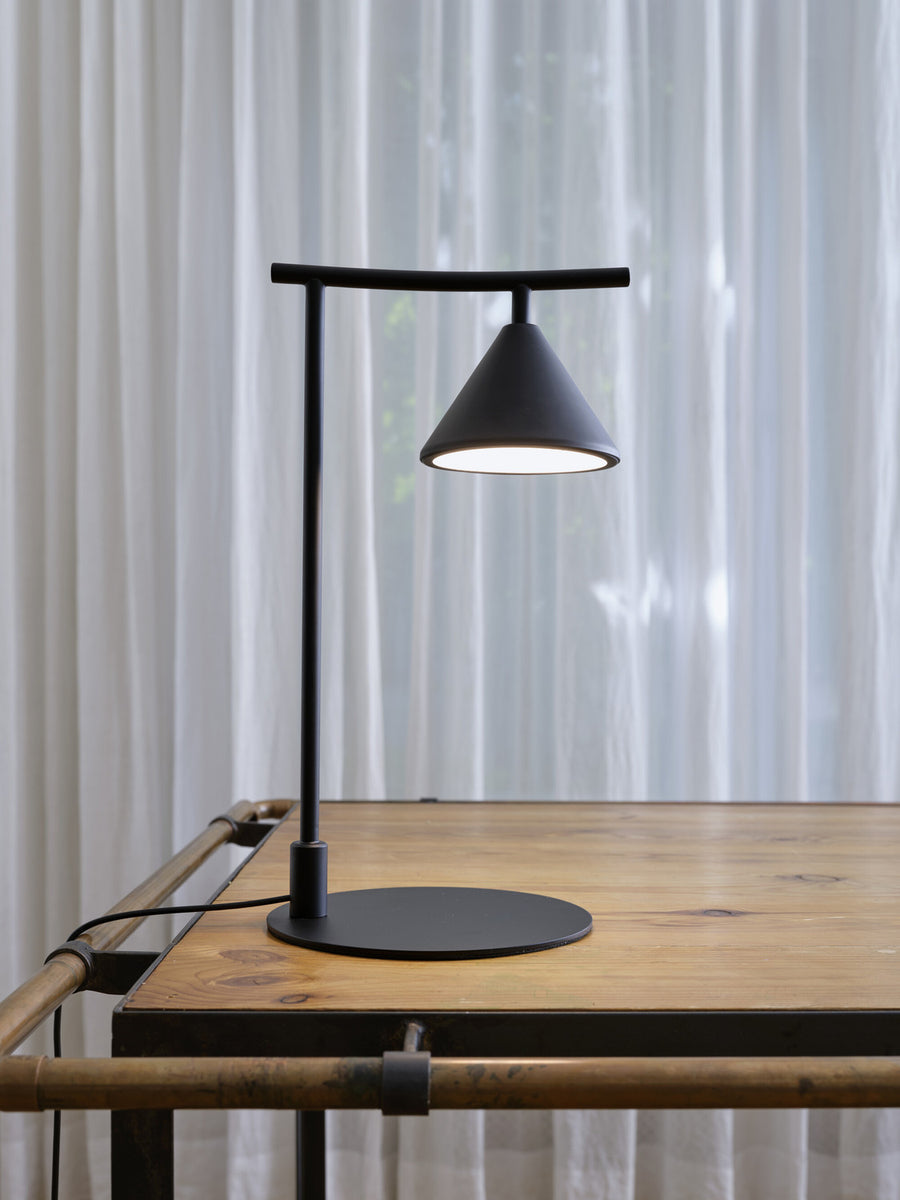 Vue rapprochée de la lampe noire allumée sur un bureau en bois, fond de rideaux.