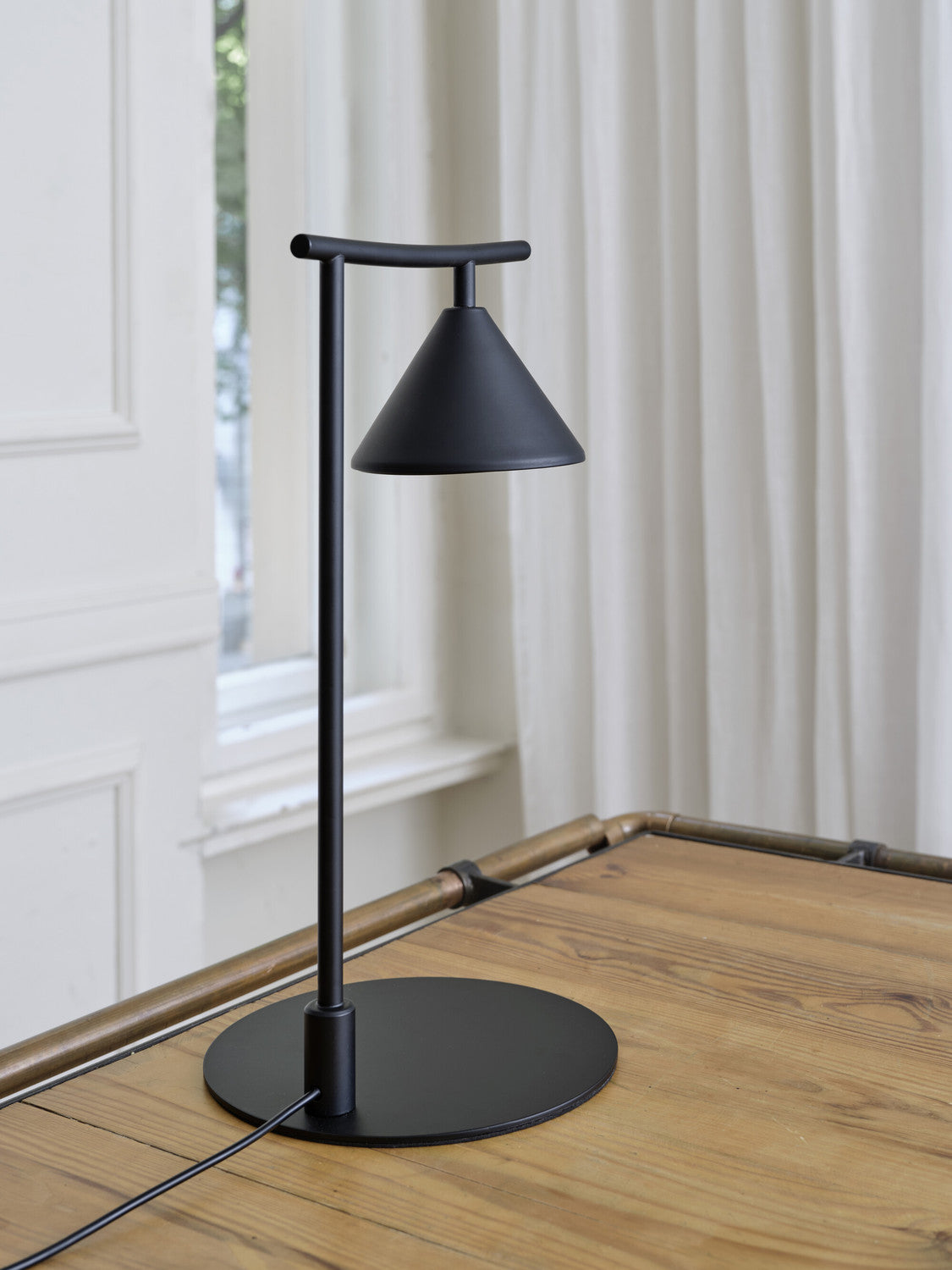 Détail de la base ronde et du pied fin sur table en bois clair.