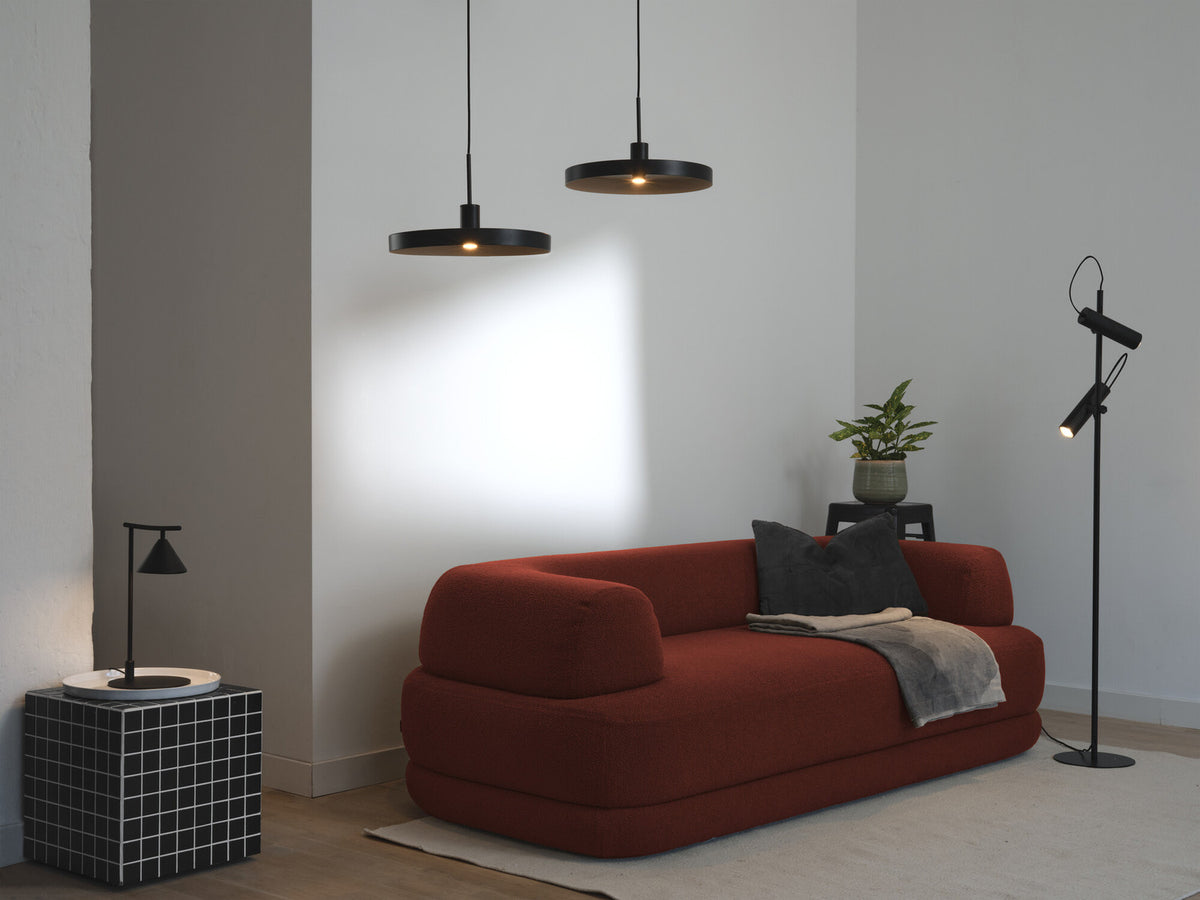 Scène de salon avec la lampe sur une table d’appoint, canapé rouge et suspensions.