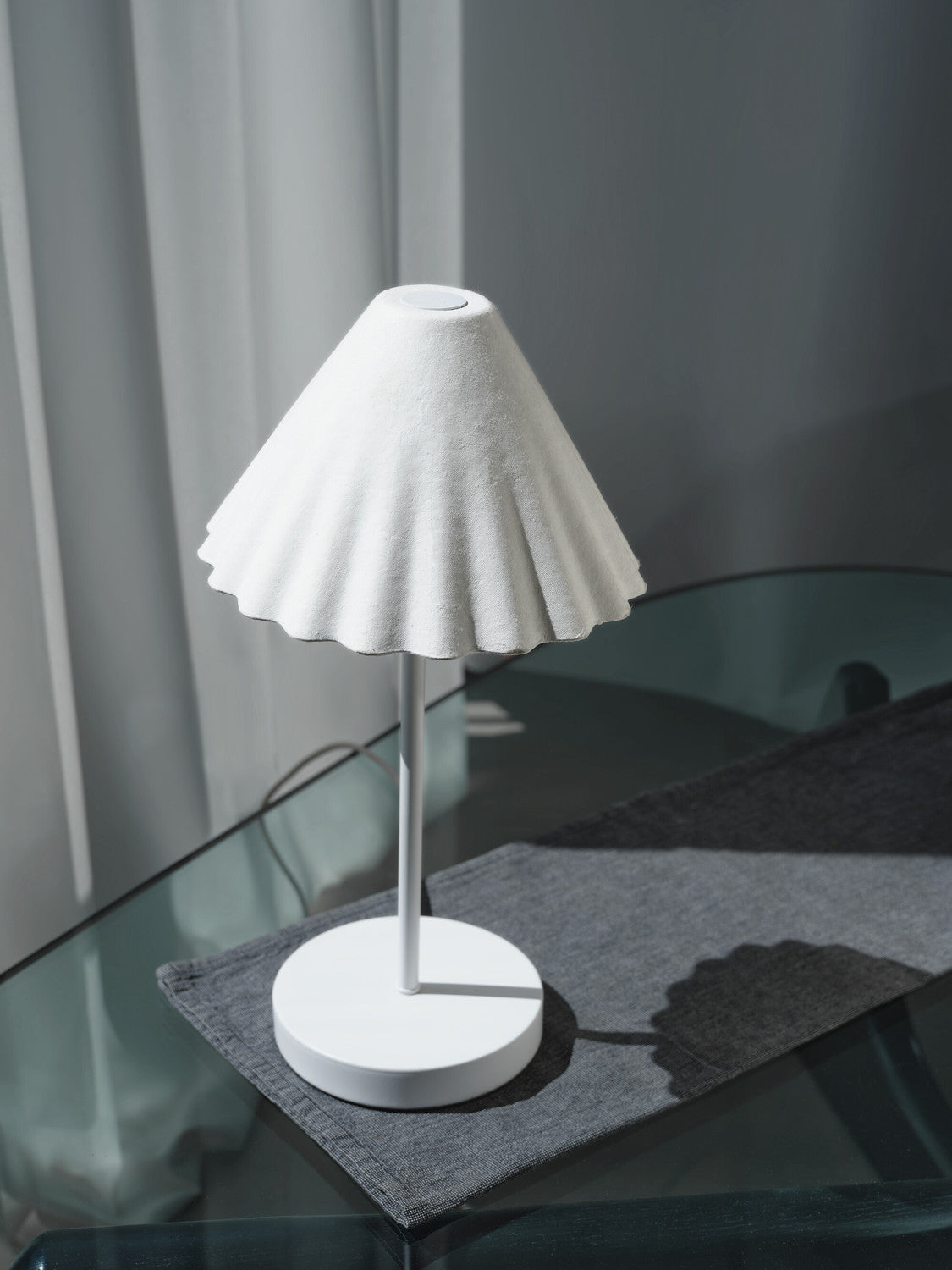 Vue rapprochée de la lampe blanche sur set gris, abat-jour plissé et finition mate.