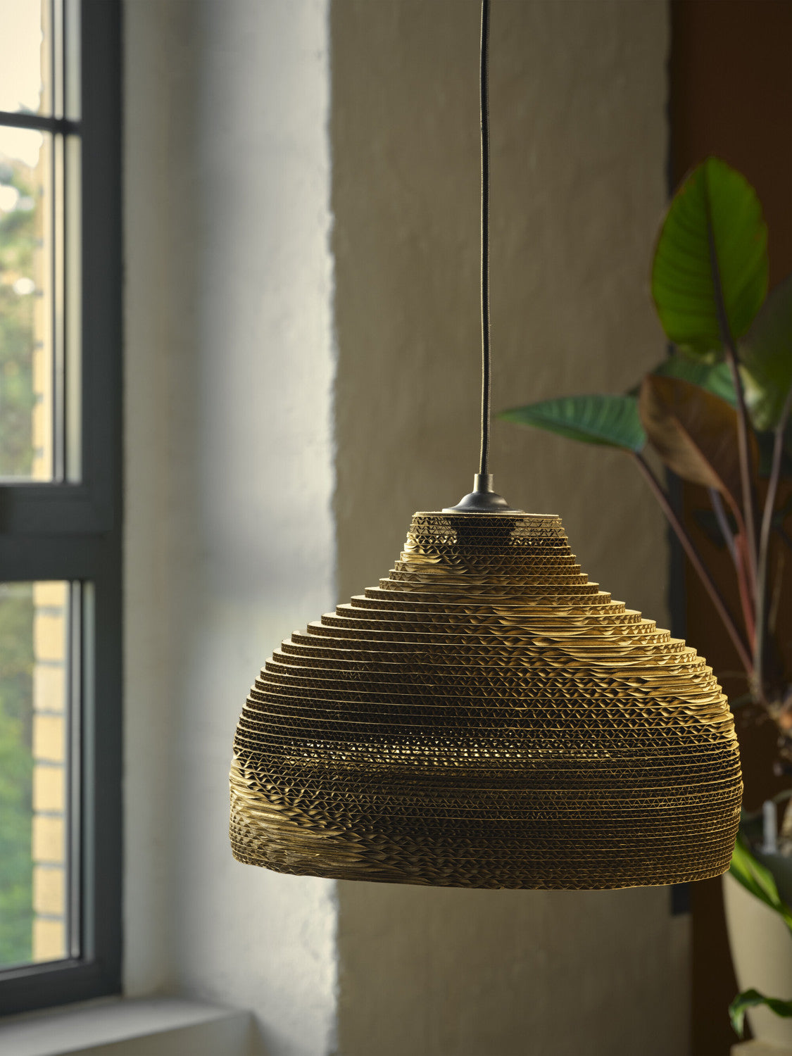 Suspension en carton suspendue près d'une fenêtre, texture ondulée éclairée par la lumière du jour.