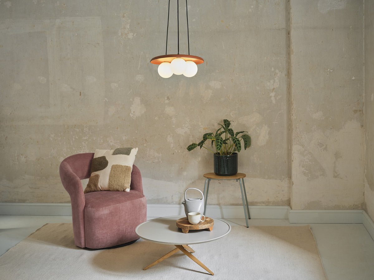 Mise en ambiance dans un salon, suspension allumée au-dessus d’un fauteuil rose.