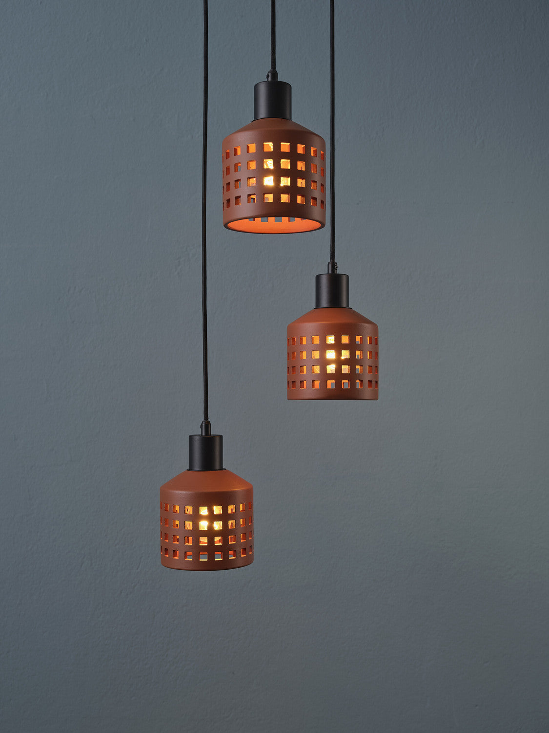 Détail rapproché des abat-jour perforés en terre cuite éclairés sur mur gris.