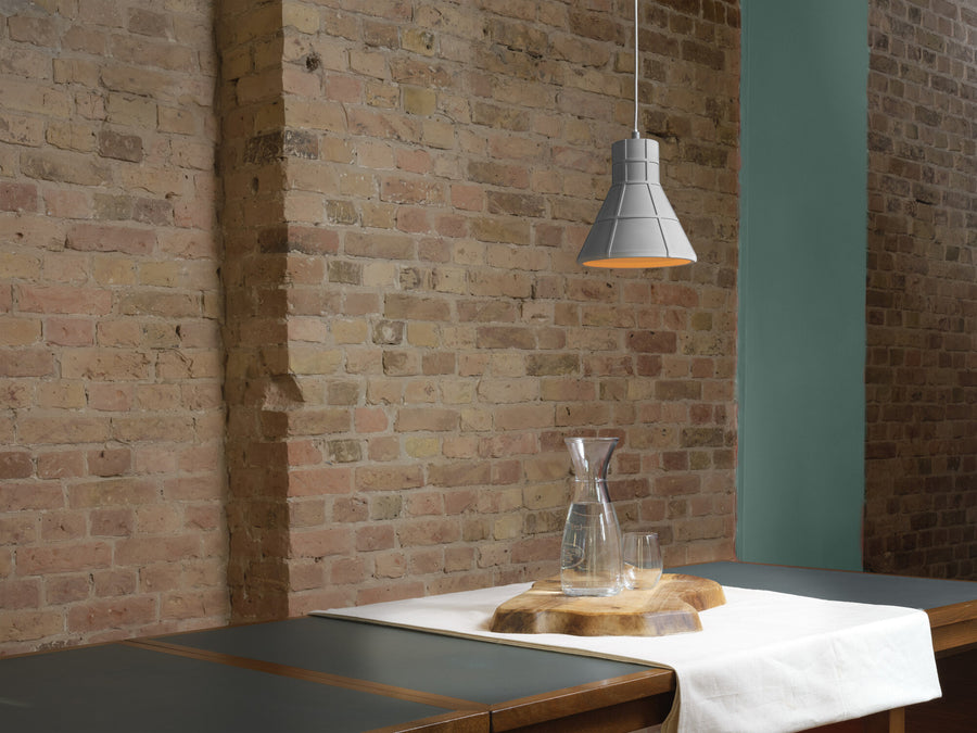 Suspension en béton éclairée au-dessus d'une table dressée devant un mur de briques.