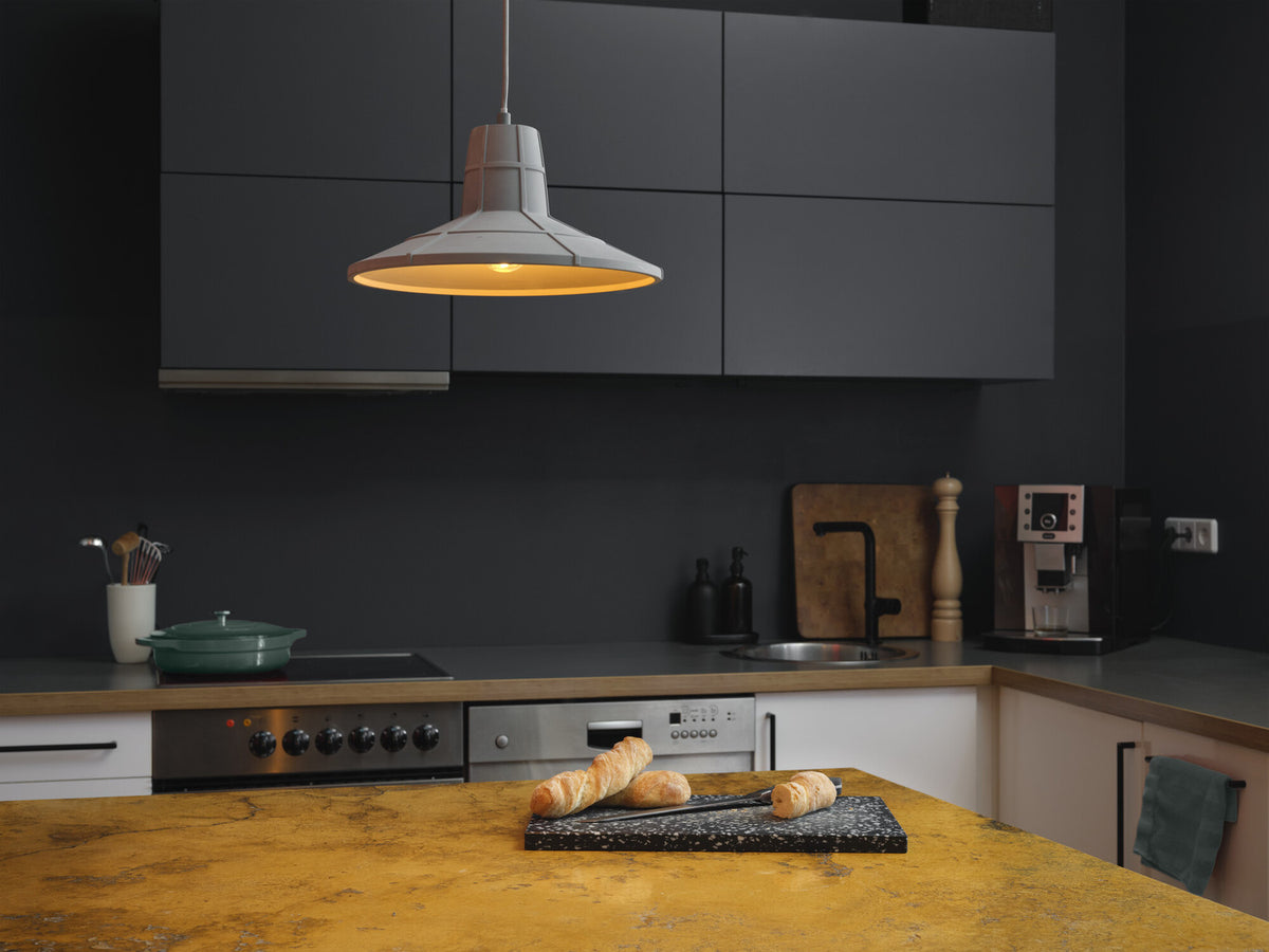 Mise en ambiance dans une cuisine sombre, suspension allumée au-dessus d'un plan de travail.