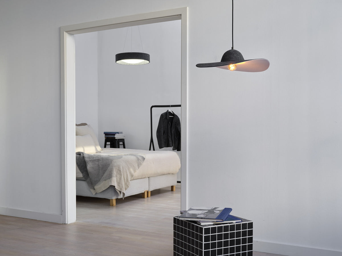 Suspension allumée dans une chambre minimaliste, vue à travers une porte blanche ouverte.