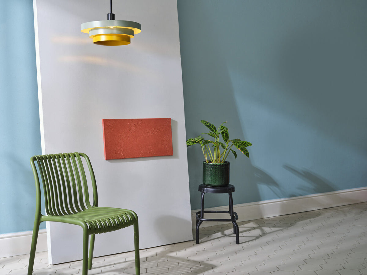 Suspension verte et jaune allumée dans un décor mural bleu avec chaise verte.
