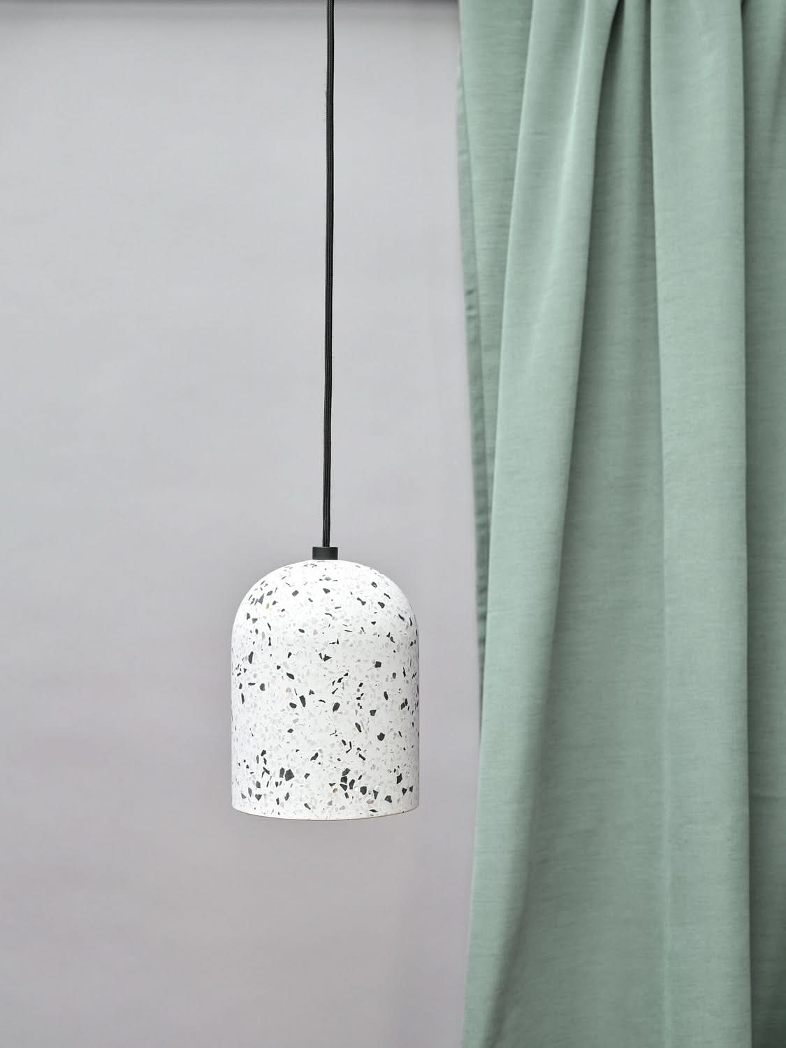Suspension terrazzo blanche devant un rideau vert clair et un mur gris.