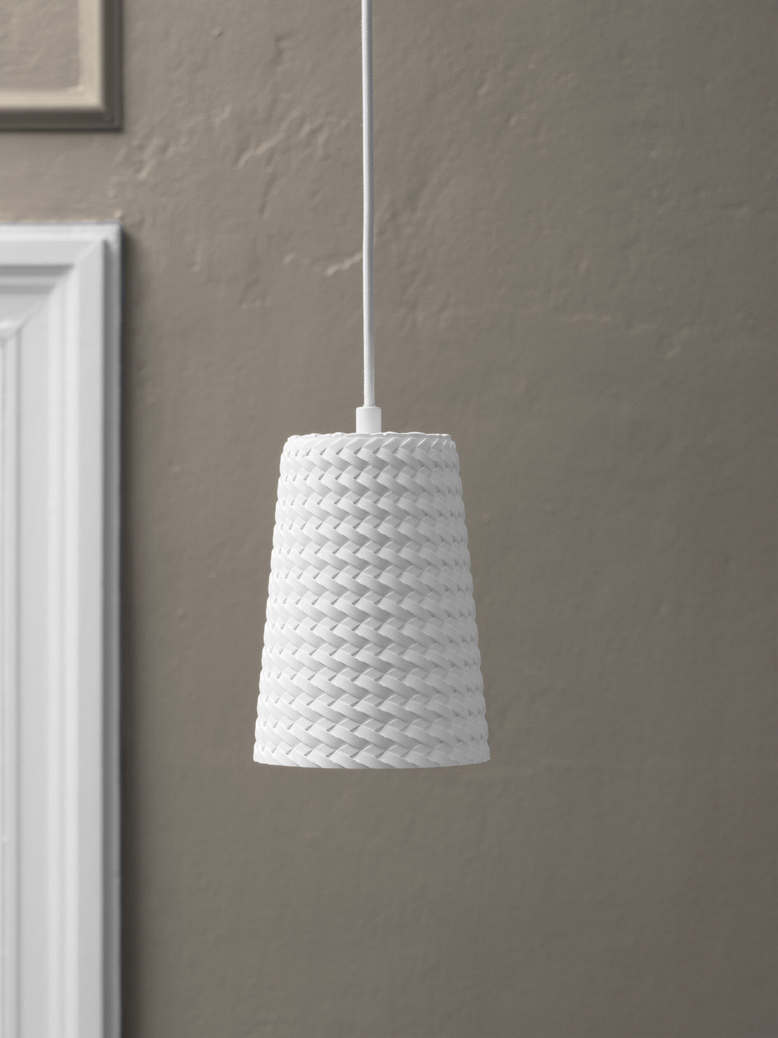 Suspension blanche devant un mur gris avec moulures, éclairage doux.