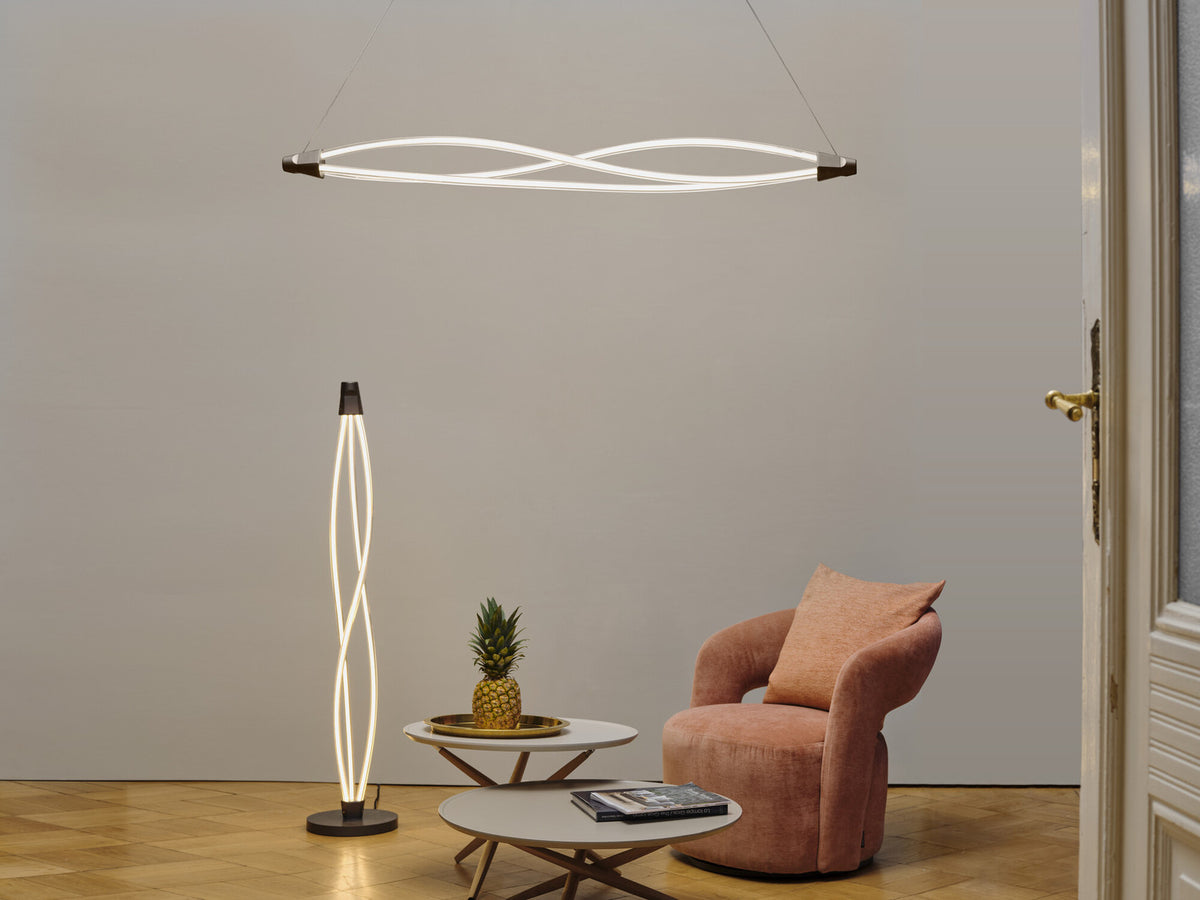 Suspension et lampe sur pied torsadées allumées dans un salon avec fauteuil rose.