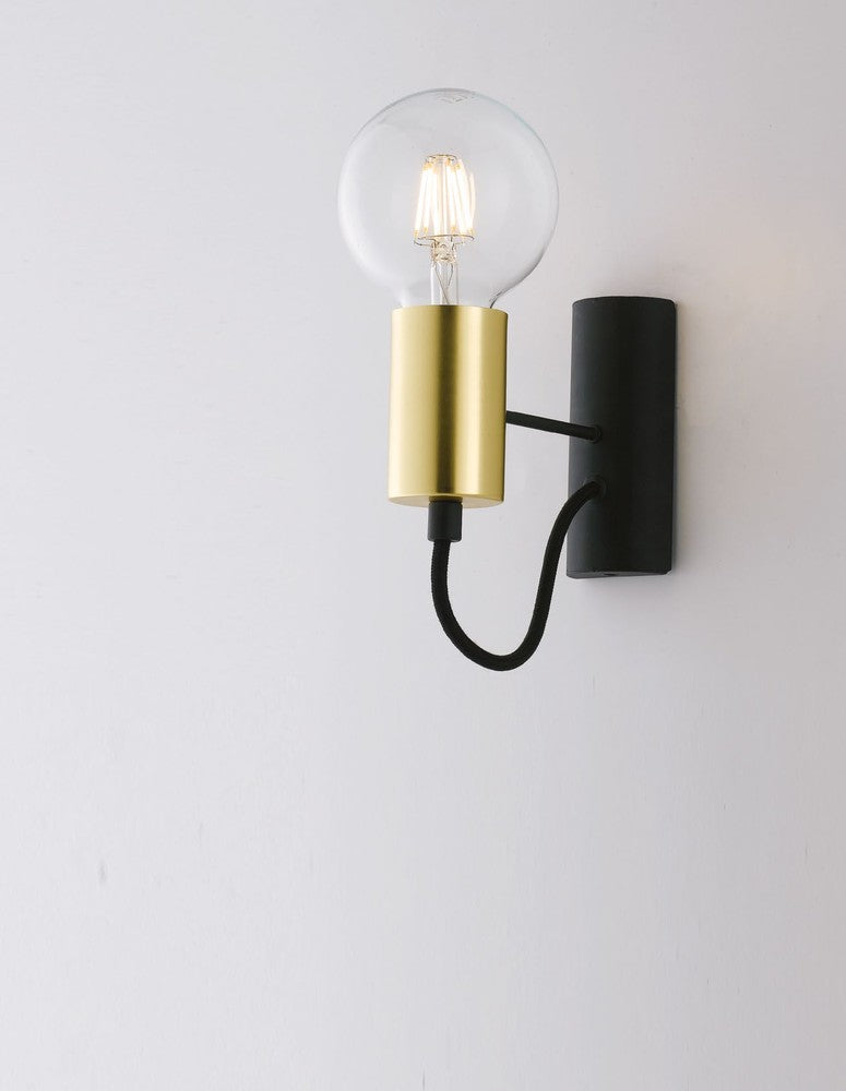 Applique noire et laiton installée sur un mur blanc, ampoule allumée en ambiance