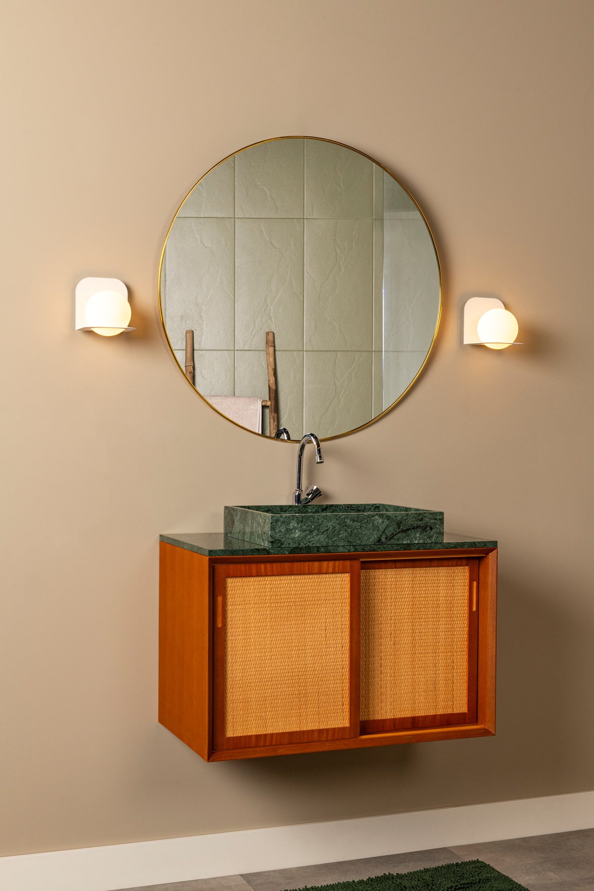 Mise en ambiance dans une salle de bain avec deux appliques murales éclairant un miroir rond.