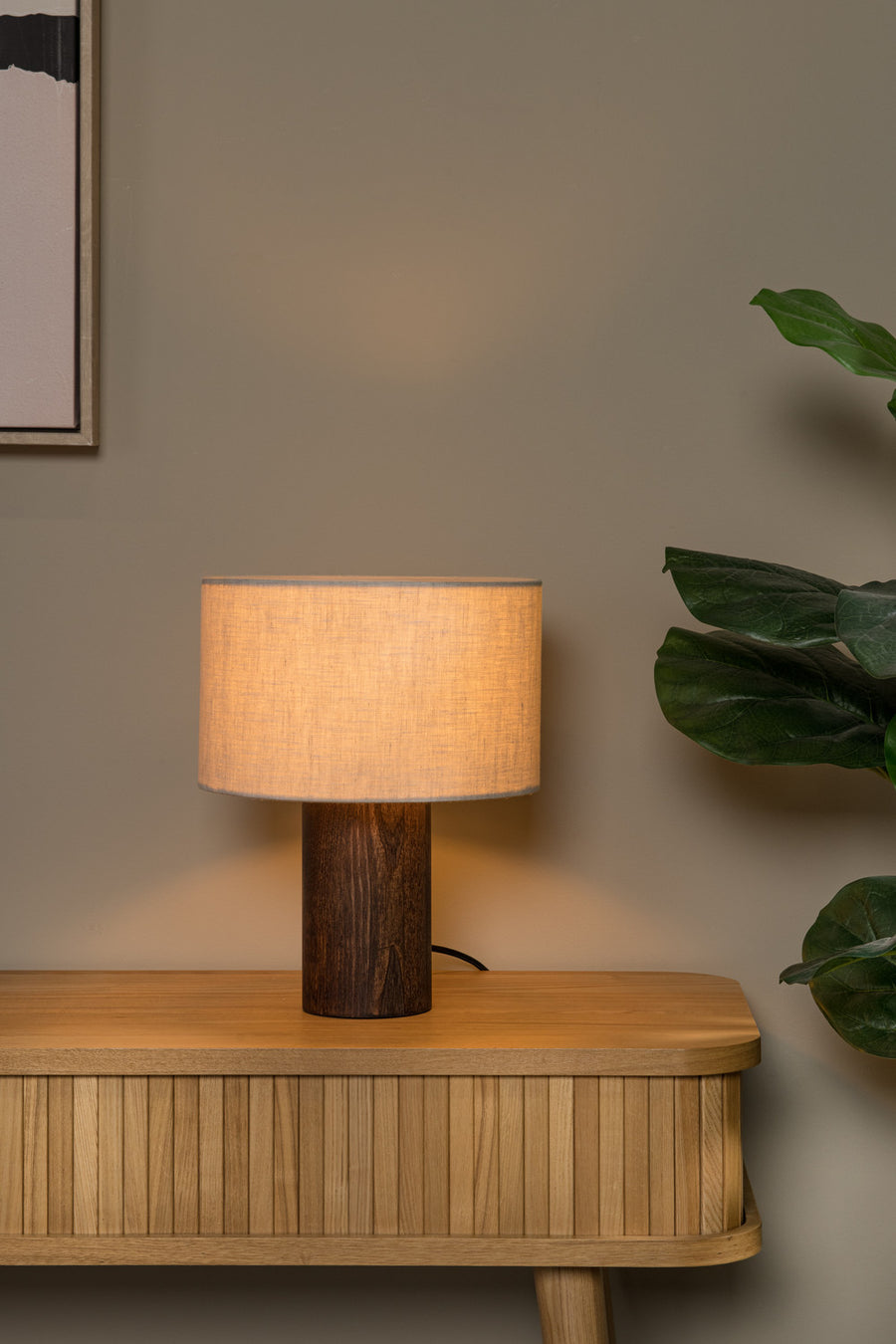 Vue rapprochée du luminaire posé sur une console en bois, feuilles vertes à droite