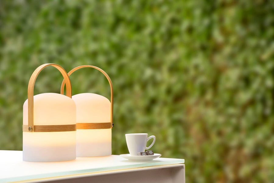Deux lampes blanches lumineuses posées sur une table, tasse à café et haie en arrière-plan