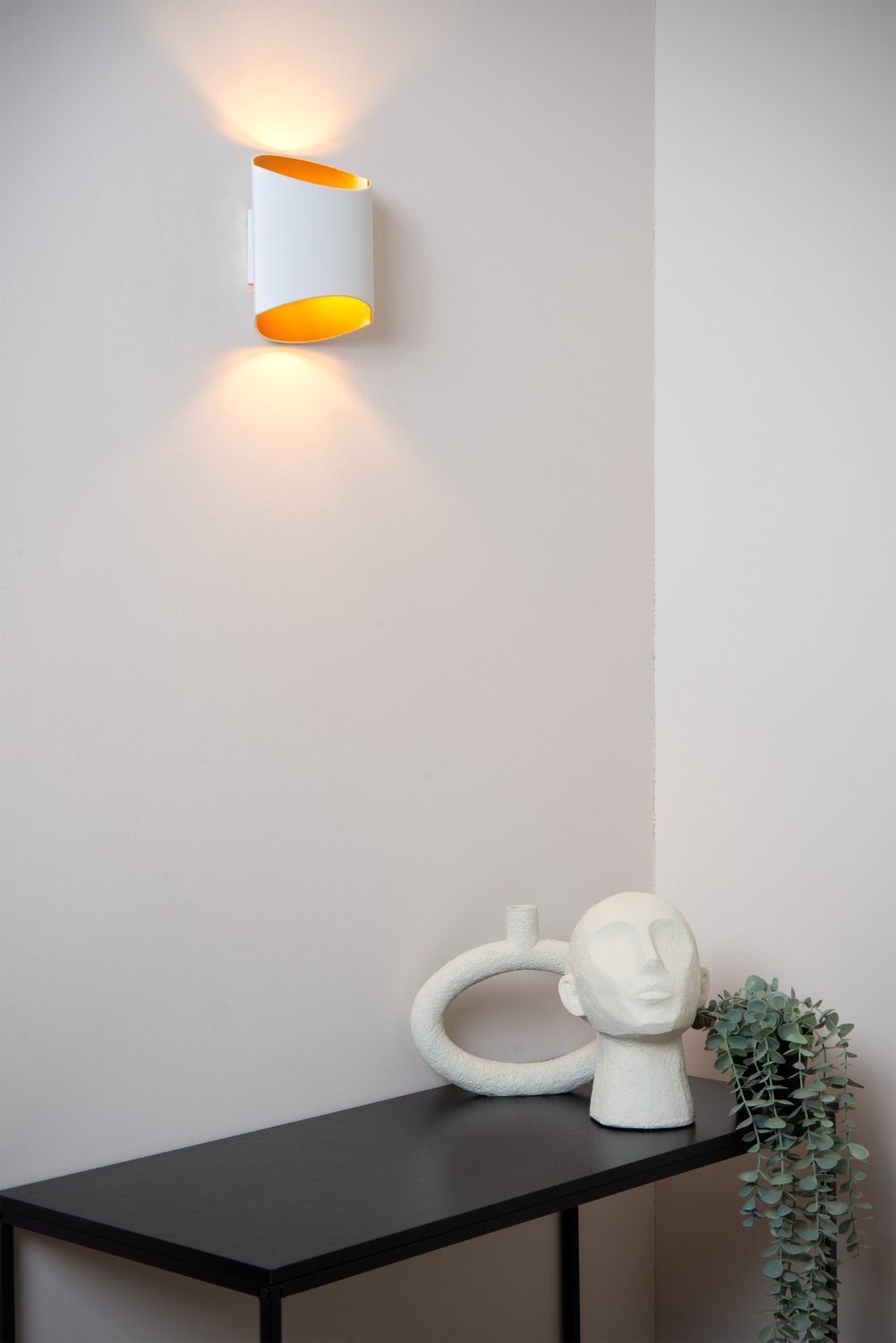 Mise en ambiance de l'applique allumée au-dessus d'une console noire avec sculptures décoratives