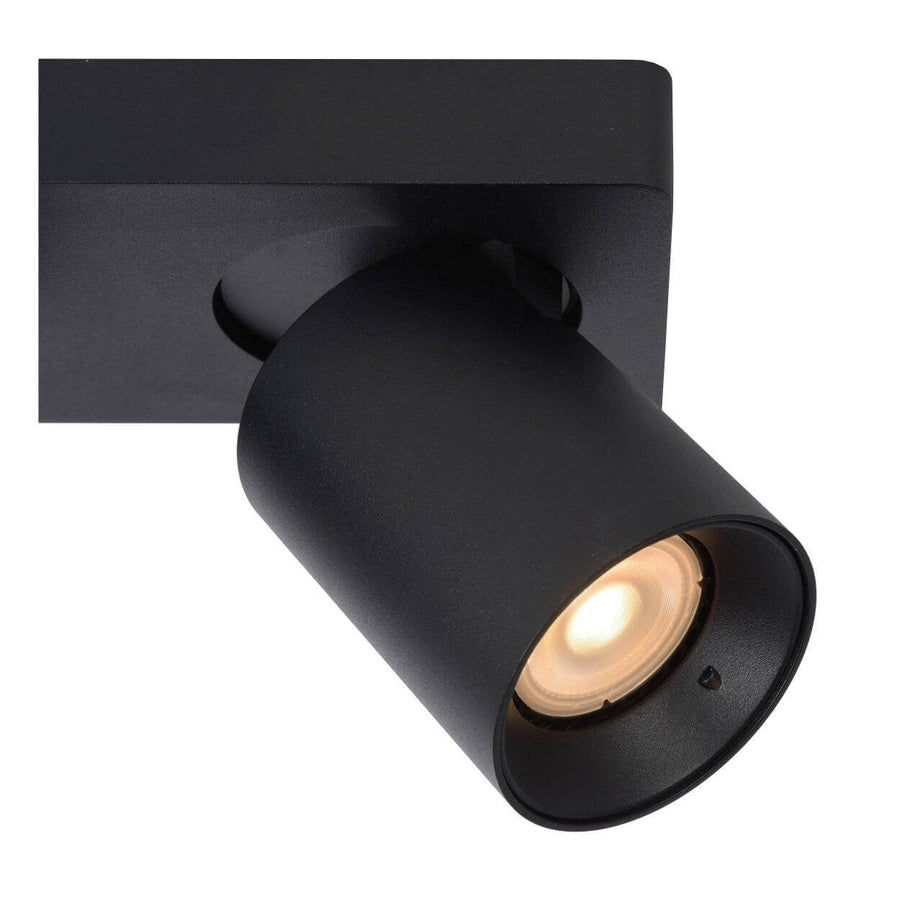 Détail en gros plan d'un spot cylindrique noir incliné, montrant l'intérieur et la lumière chaude.