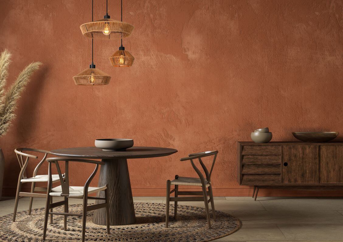 Mise en ambiance sur mur terracotta, suspension en rotin au-dessus d'une table en bois