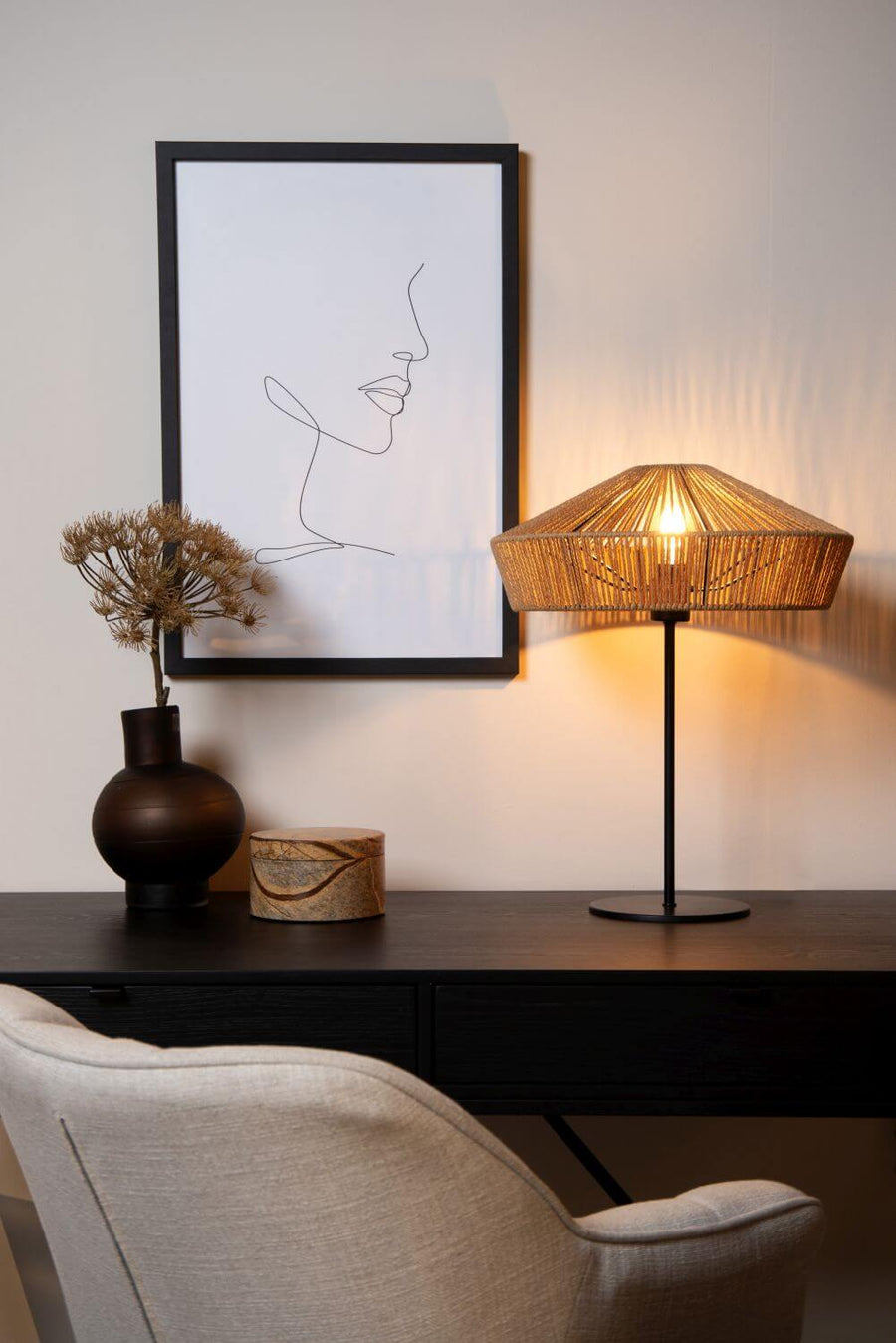 Lampe posée sur un bureau devant un fauteuil beige et une affiche encadrée