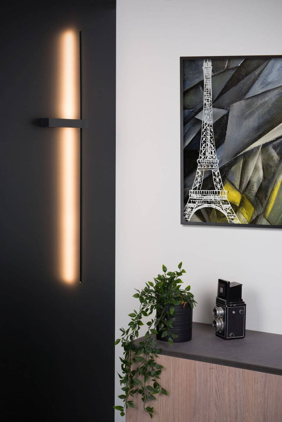 Vue rapprochée de l'applique murale noire allumée devant un mur sombre et une toile.