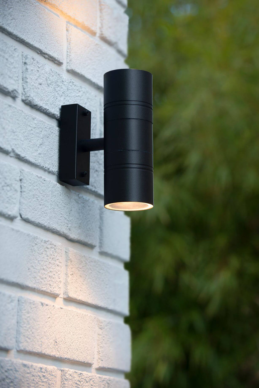 Vue rapprochée du luminaire noir éclairant vers le bas devant une haie verte