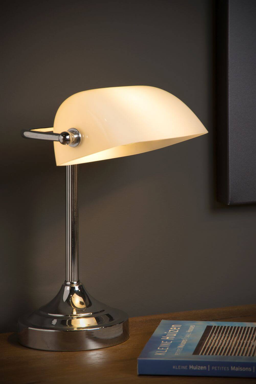 Mise en ambiance nocturne sur bureau en bois, lampe allumée près d’un livre.
