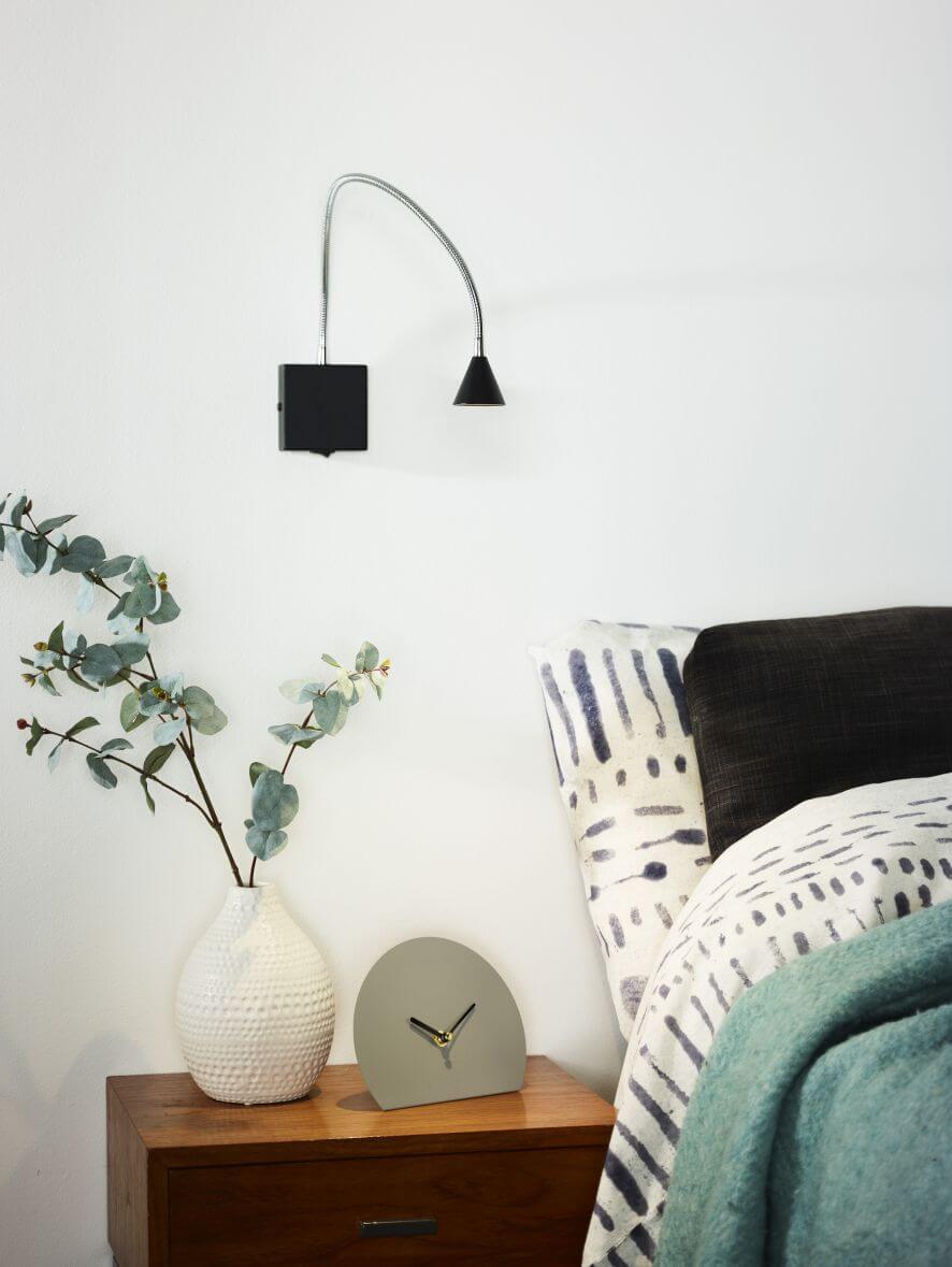 Applique murale noire et chromée installée au-dessus d'une table de nuit dans une chambre.